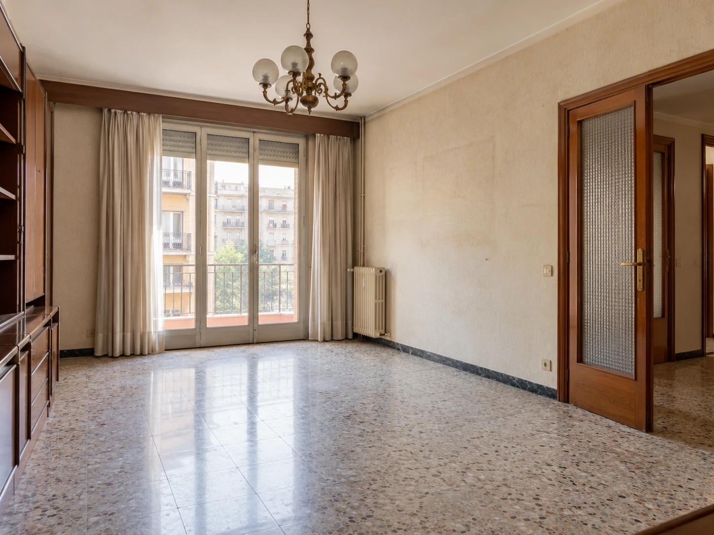 Salón de un piso en Barcelona con suelo de terrazo, carpintería de madera y lámpara clásica, antes de una reforma integral