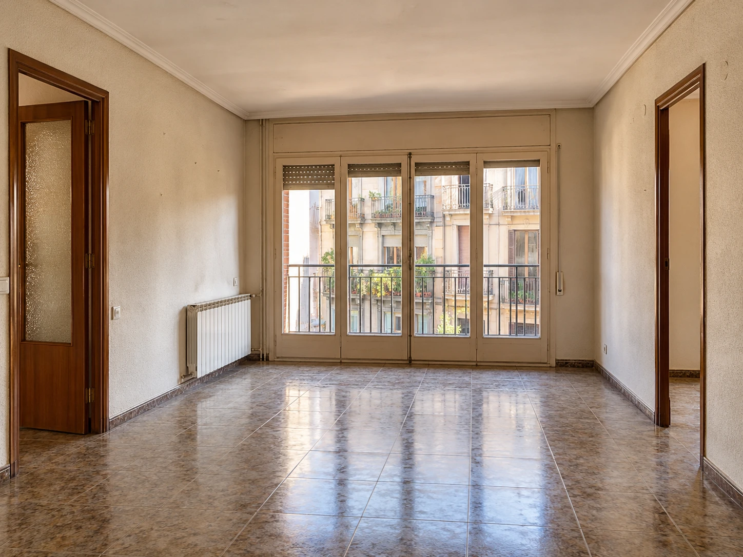 Salón vacío de una vivienda con balcón a la calle, listo para reformar antes de mudarse
